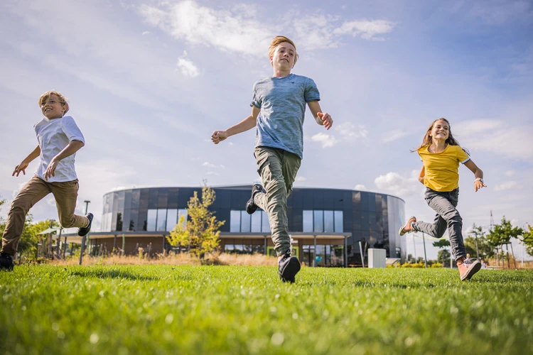 Kinder rennen auf der Wiese im Themenpark. Im Hintergrund sieht man die KLIMA ARENA.