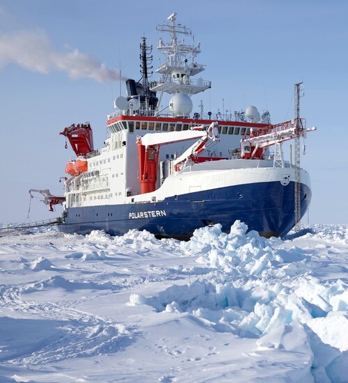 Der Eisbrecher Polarstern im arktischen Eis und drei Wissenschaftler stehen in Eisfeld davor.